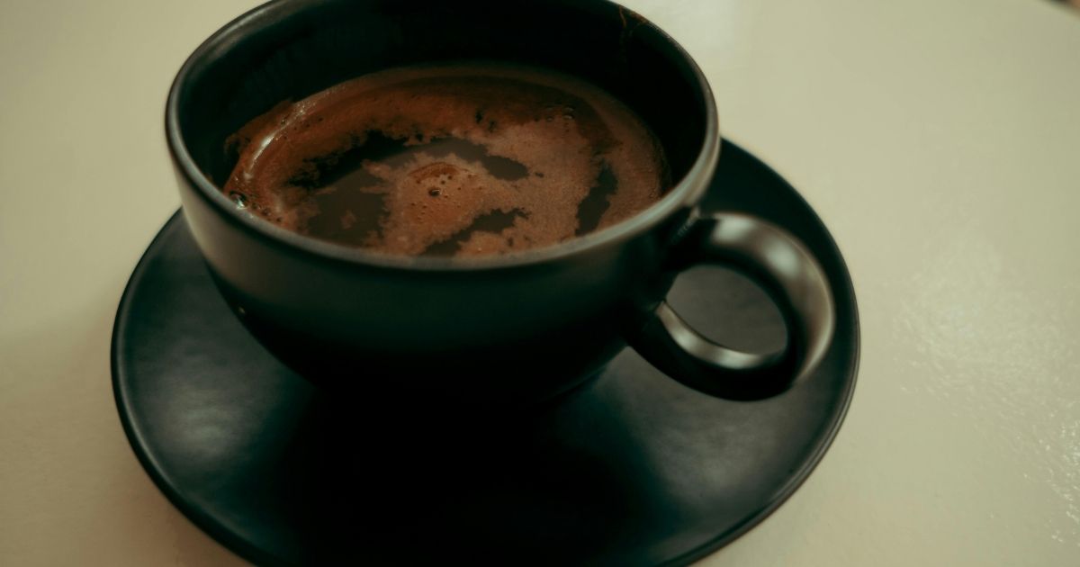 Black coffee in a simple cup next to a clock representing an intermittent fasting window