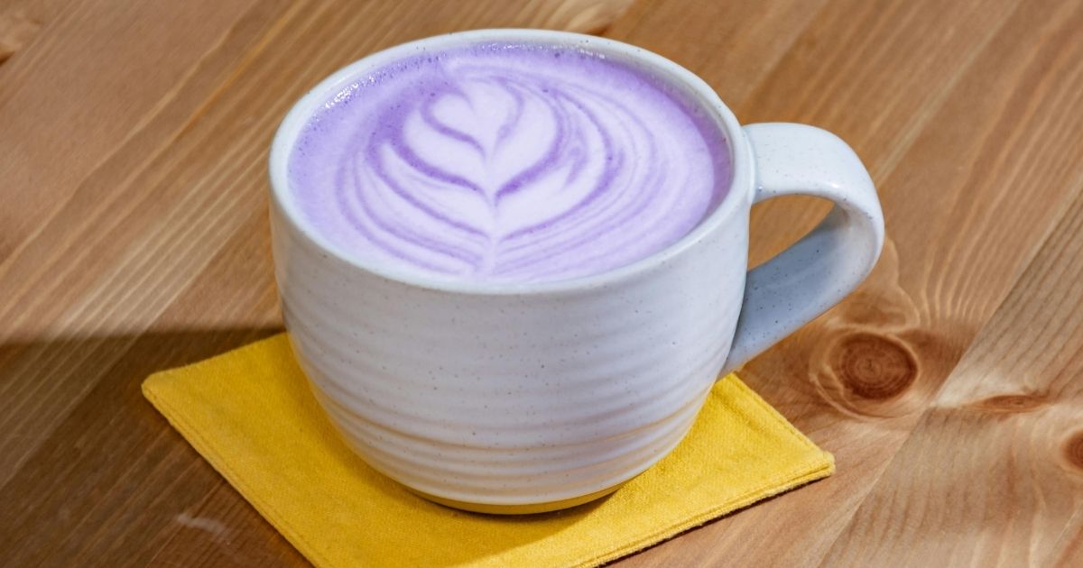 A vibrant purple ube latte in a clear glass showing the layered purple and white colors